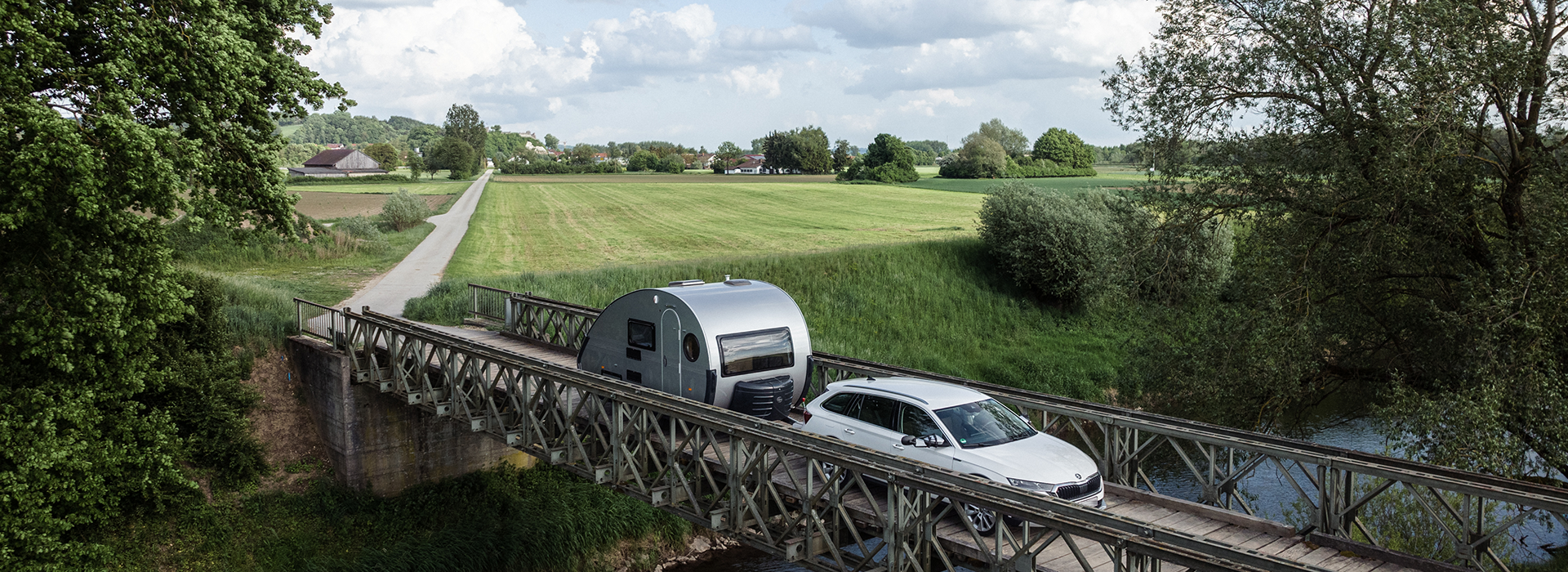 T@b Wohnwagen auf grüner Landschaft, wird von einem Auto gezogen